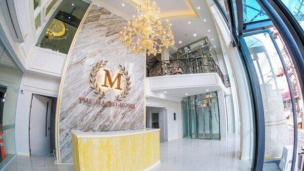 A hotel reception area with a marble wall, a chandelier, and a glass elevator. - The MACEO Hotel (Nong Khai)