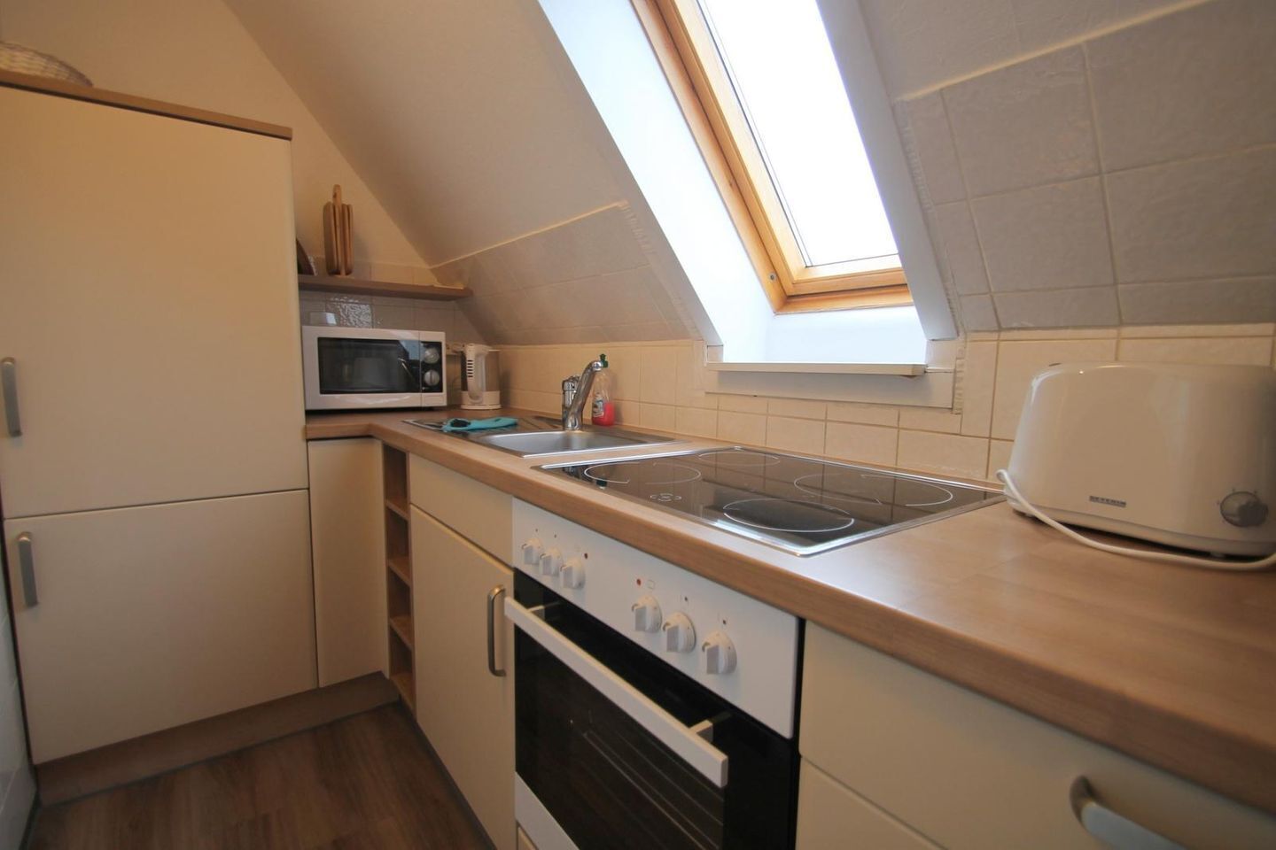 A compact kitchen with a microwave, stove, oven, and a skylight.
