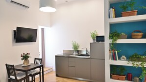 A modern kitchen with a built-in stove, a dining area with a table and chairs, and a bookshelf with plants and books. - At Home Montebello (Rome)