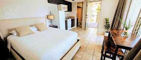 A hotel room with a bed, a desk, a microwave, a refrigerator, and a potted plant.
