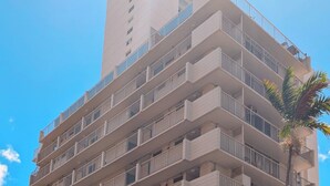 Un hotel de varios pisos con balcones, un área de estacionamiento y una palmera.