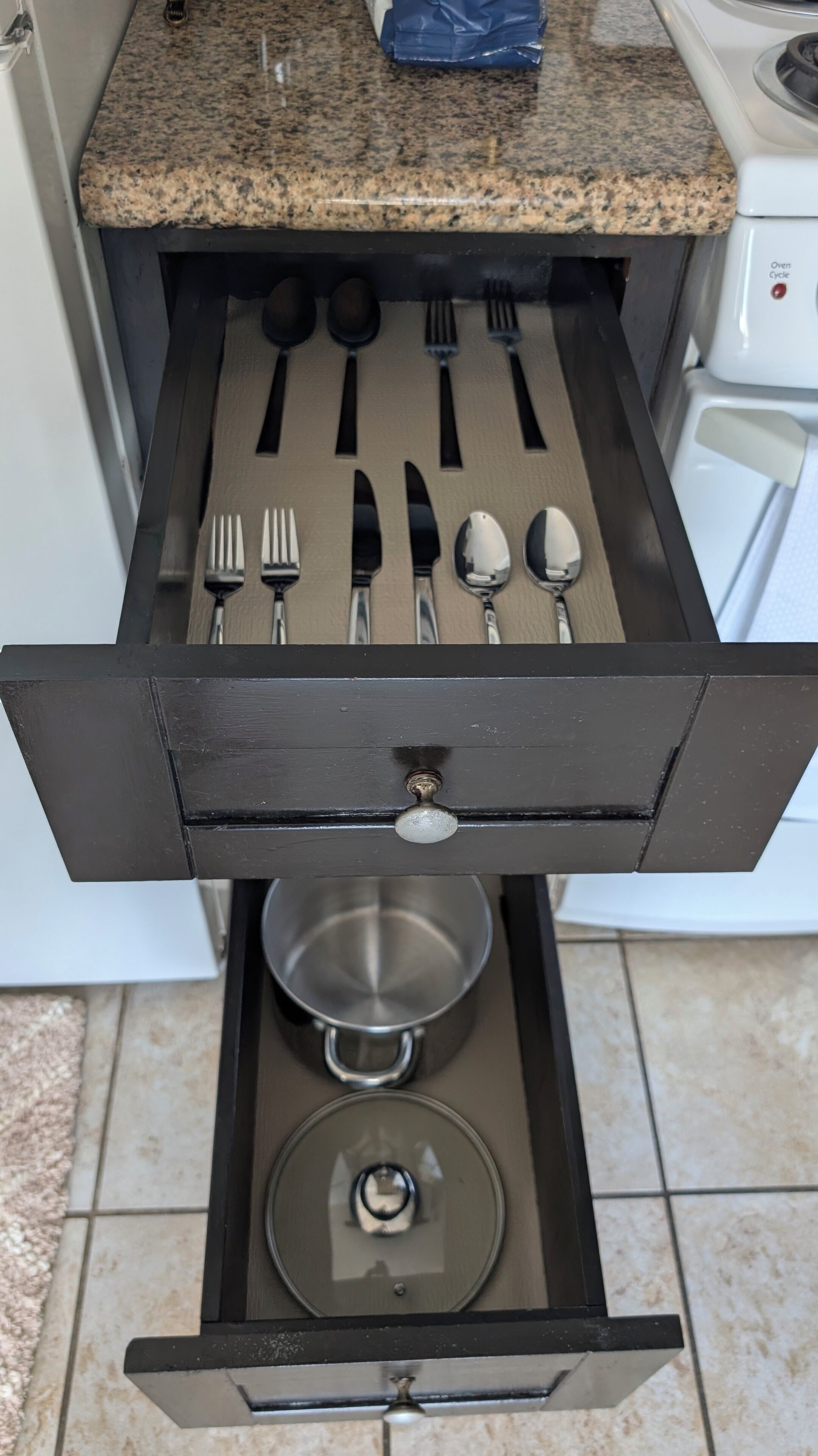 A kitchen drawer with utensils and a pot.