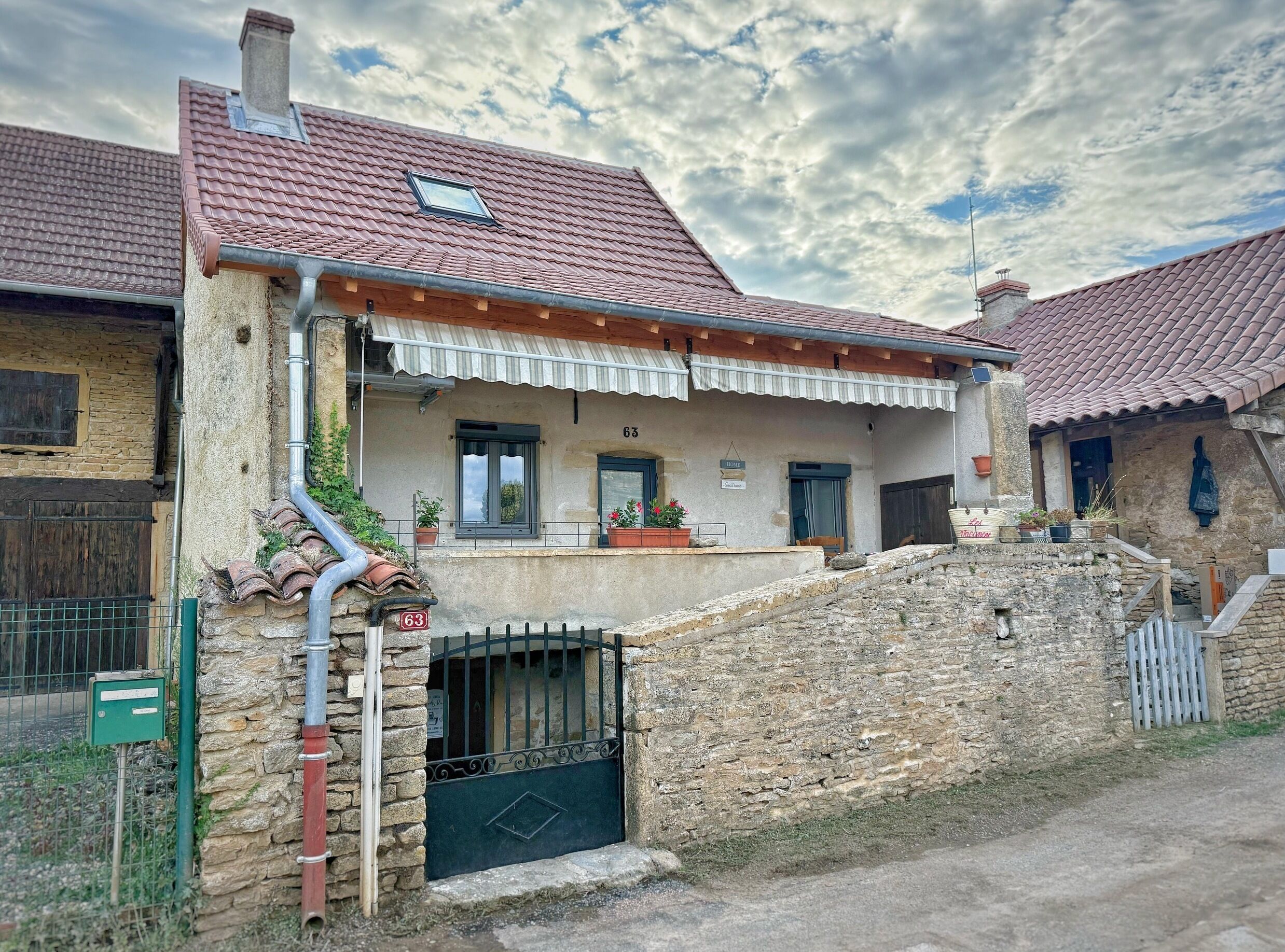 Una casa de piedra tradicional con techo de tejas, un porche pequeño y un muro de piedra.