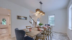A dining area with a wooden table set for six, surrounded by six chairs. A staircase is visible in the background leading to another room.