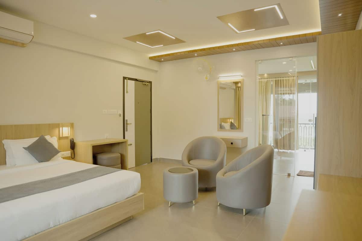 A modern hotel room with a large bed, two armchairs, a small table, and a mirror.