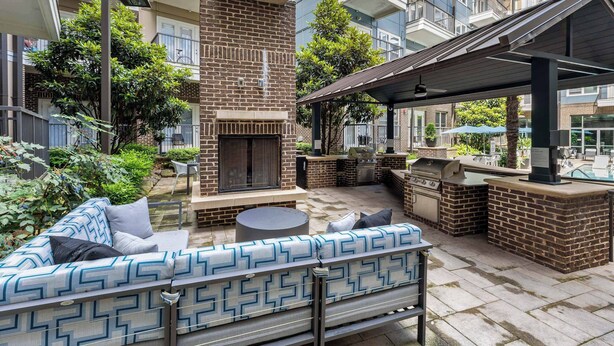 An outdoor patio area with a brick fireplace, outdoor seating, and a covered barbecue area. - CPCC Area Escape | Pool Gym Parking Balcony (Charlotte)