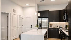 A modern kitchen with a central island, dark cabinetry, stainless steel appliances, and a white countertop. - CPCC Area Escape | Pool Gym Parking Balcony (Charlotte)