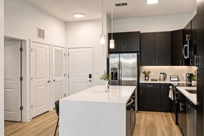 A modern kitchen with a central island, dark cabinetry, stainless steel appliances, and a white countertop. - CPCC Area Escape | Pool Gym Parking Balcony (Charlotte)