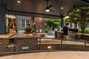 An outdoor patio area with a brick counter, seating, and a grill station. - CPCC Area Escape | Pool Gym Parking Balcony (Charlotte)