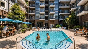 A swimming pool with lounge chairs and umbrellas, surrounded by a multi-story building with balconies. - CPCC Area Escape | Pool Gym Parking Balcony (Charlotte)