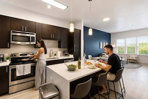 A modern kitchen with dark cabinets, stainless steel appliances, and a central island with seating. - CPCC Area Escape | Pool Gym Parking Balcony (Charlotte)