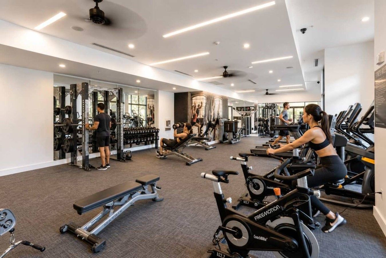 Un gimnasio con máquinas de cardio, pesas libres y un espejo grande.