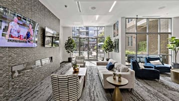 A modern hotel lobby with a seating area, a TV screen, and large windows.