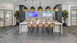 A modern hotel lobby with a reception desk, multiple bar stools, and two large screens displaying 'NEWSLIVE' and 'WE'LL BE RIGHT BACK'. - CPCC Area Escape | Pool Gym Parking Balcony (Charlotte)