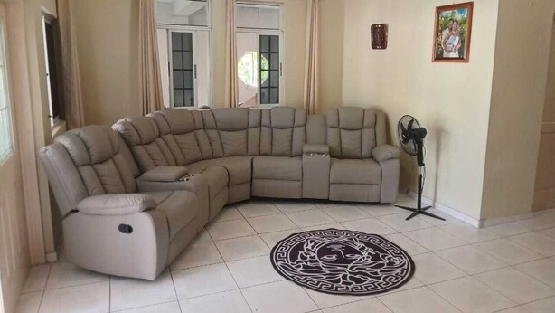 A living room with a beige sectional sofa, a standing fan, and a decorative rug.