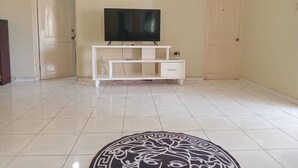 A living room with a flat-screen TV on a white entertainment unit, a patterned rug on the floor, and two framed pictures on the wall.