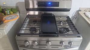 A stainless steel stove with a digital control panel, four burners, and a range hood.