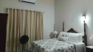 A bedroom with a bed, curtains, a fan, and a wall-mounted air conditioner.