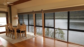 Un coin repas avec une grande fenêtre donnant sur un lac, des meubles en bois et un ventilateur de plafond.