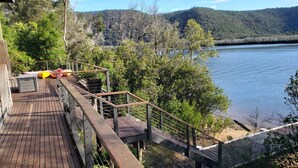 Une terrasse en bois dotée d’une balustrade, qui offre une vue sur un lac, et qui est entourée d’arbres et de collines.