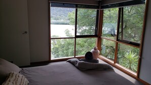 Une chambre avec une grande fenêtre, un lit et un vase posé sur le rebord de la fenêtre.