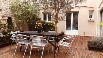 A wooden deck with a table and chairs, surrounded by plants and a tree.