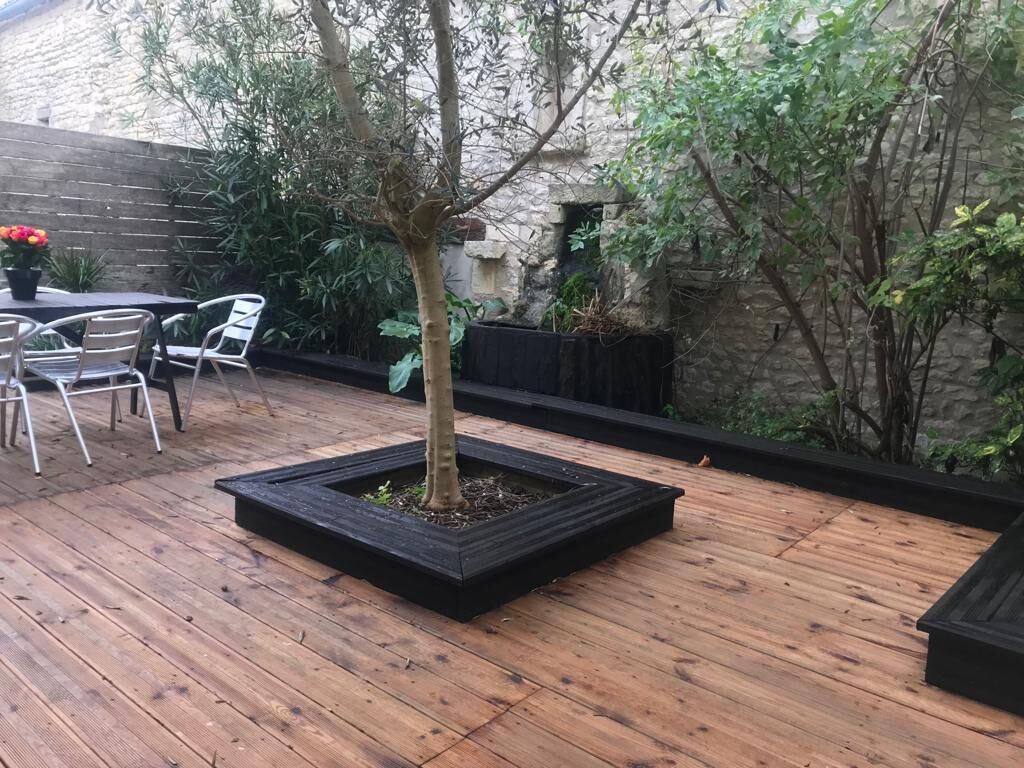 A wooden deck with a small tree planter, outdoor seating, and a stone wall.