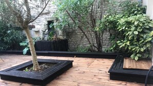 Una terraza de madera con tres macetas cuadradas que contienen árboles y un arbusto.