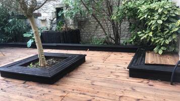 Una terraza de madera con tres macetas cuadradas que contienen árboles y un arbusto.