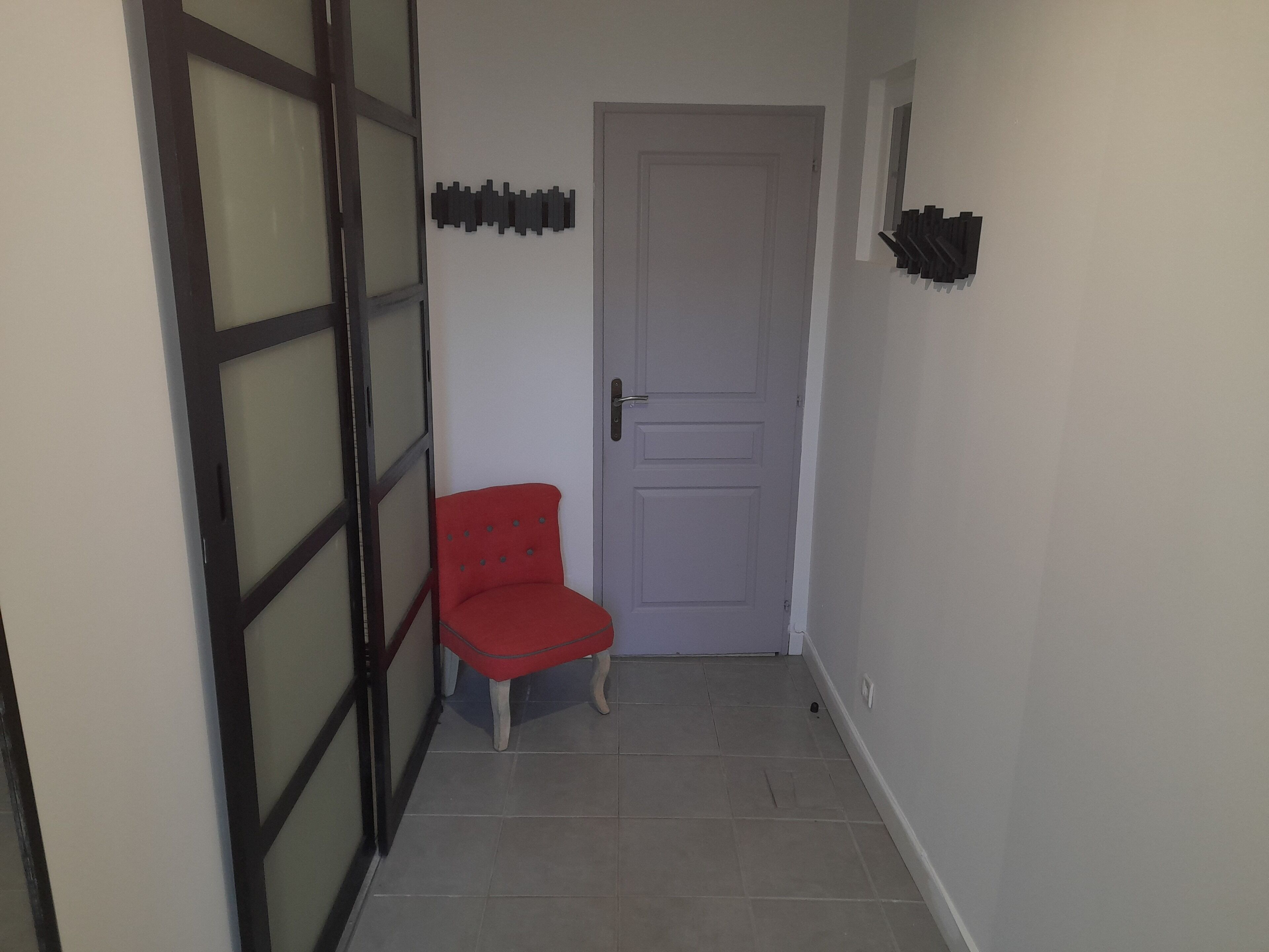 Um corredor estreito com uma cadeira vermelha, uma porta branca e uma prateleira fixada na parede.