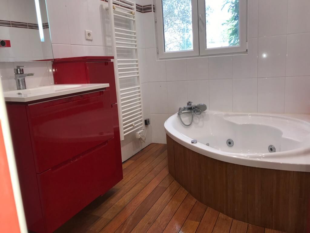 Un bagno moderno con pavimento in legno, una console bianca, una vasca da bagno bianca e una finestra che offre luce naturale.