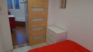 Un dormitorio con un armario de madera, una mesita de noche pequeña y una colcha roja.
