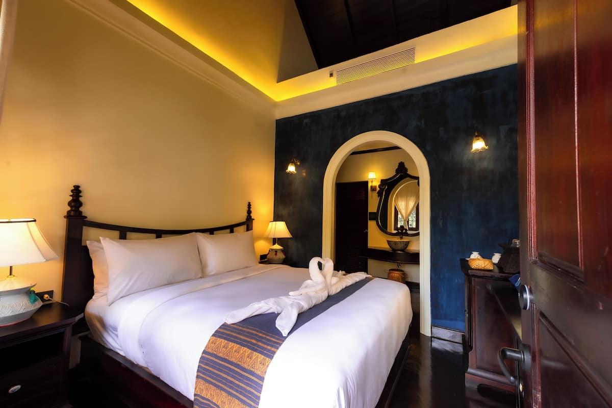 A hotel room with a neatly made bed, a nightstand with a lamp, and a wooden wardrobe.