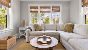 A living room with a beige sectional sofa, a round wooden coffee table with a decorative item, and a window with a view of trees and a house. - 5 Minutes to Beach|Newly Furnished Designer Home (Mount Pleasant)