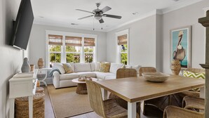 A modern living room with a sofa, dining table, wicker chairs, a flat-screen TV, and a ceiling fan. - 5 Minutes to Beach|Newly Furnished Designer Home (Mount Pleasant)