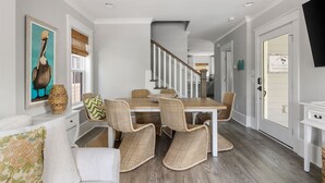 A dining area with a wooden table and wicker chairs, a white sofa with patterned cushions, and a painting on the wall. - 5 Minutes to Beach|Newly Furnished Designer Home (Mount Pleasant)