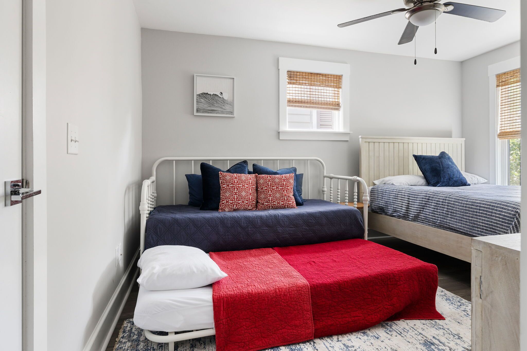 A bedroom with two beds, a ceiling fan, a window with blinds, and a wall-mounted light switch.