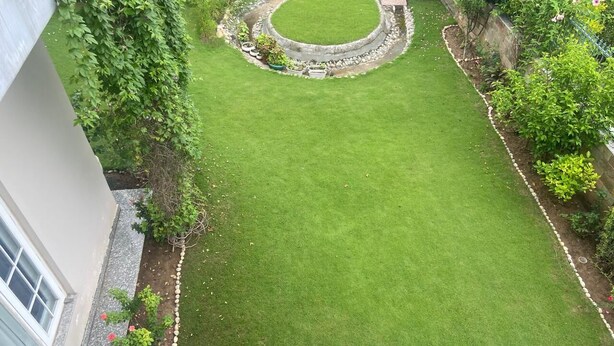 A well-maintained lawn with a circular stone feature, bordered by a low stone wall, and surrounded by various plants and shrubs. - IT City Homestay-Secure & Comfortable Stay in Mohali (Sahibzada Ajit Singh Nagar)