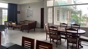 A spacious living area with a dining table and chairs, a sofa set, and a large window with a view of buildings and greenery. - IT City Homestay-Secure & Comfortable Stay in Mohali (Sahibzada Ajit Singh Nagar)