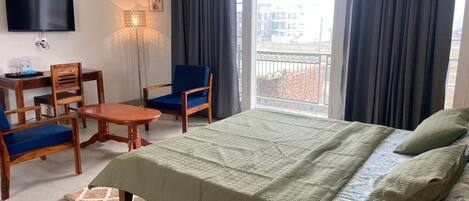 Habitación de hotel con cama, escritorio, silla, televisor y ventana con cortinas.