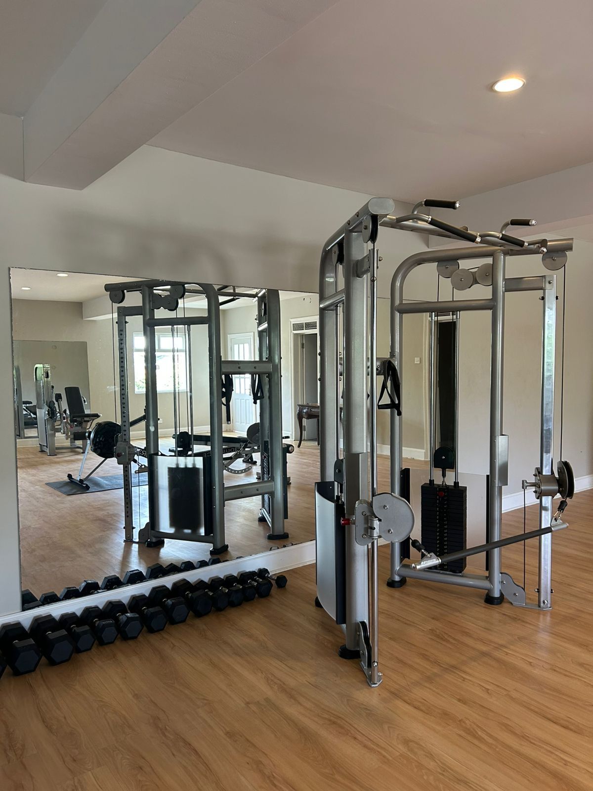 A gym with weightlifting equipment, mirrors, and a wooden floor.