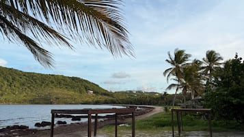 A wooden structure with a bench, a path leading to a beach, and palm trees in the background.