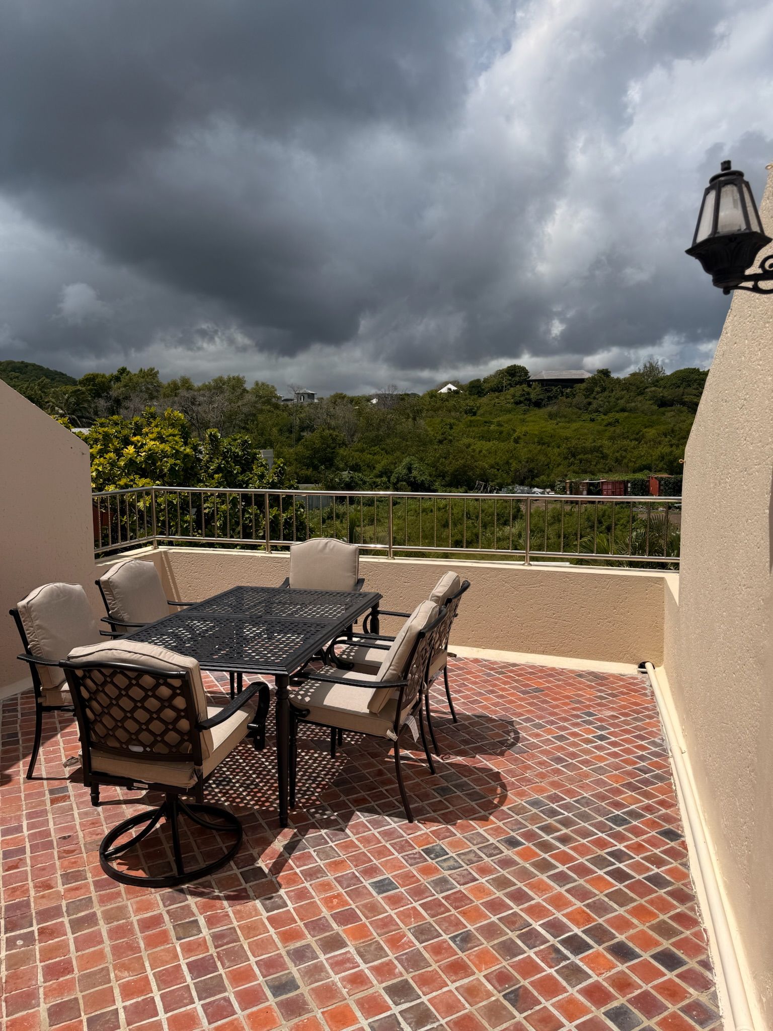 Une terrasse extérieure avec une table et des chaises, un sol carrelé et une vue sur un paysage vallonné sous un ciel nuageux.