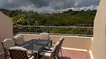 Une terrasse extérieure avec une table et des chaises, un sol carrelé et une vue sur un paysage vallonné sous un ciel nuageux.