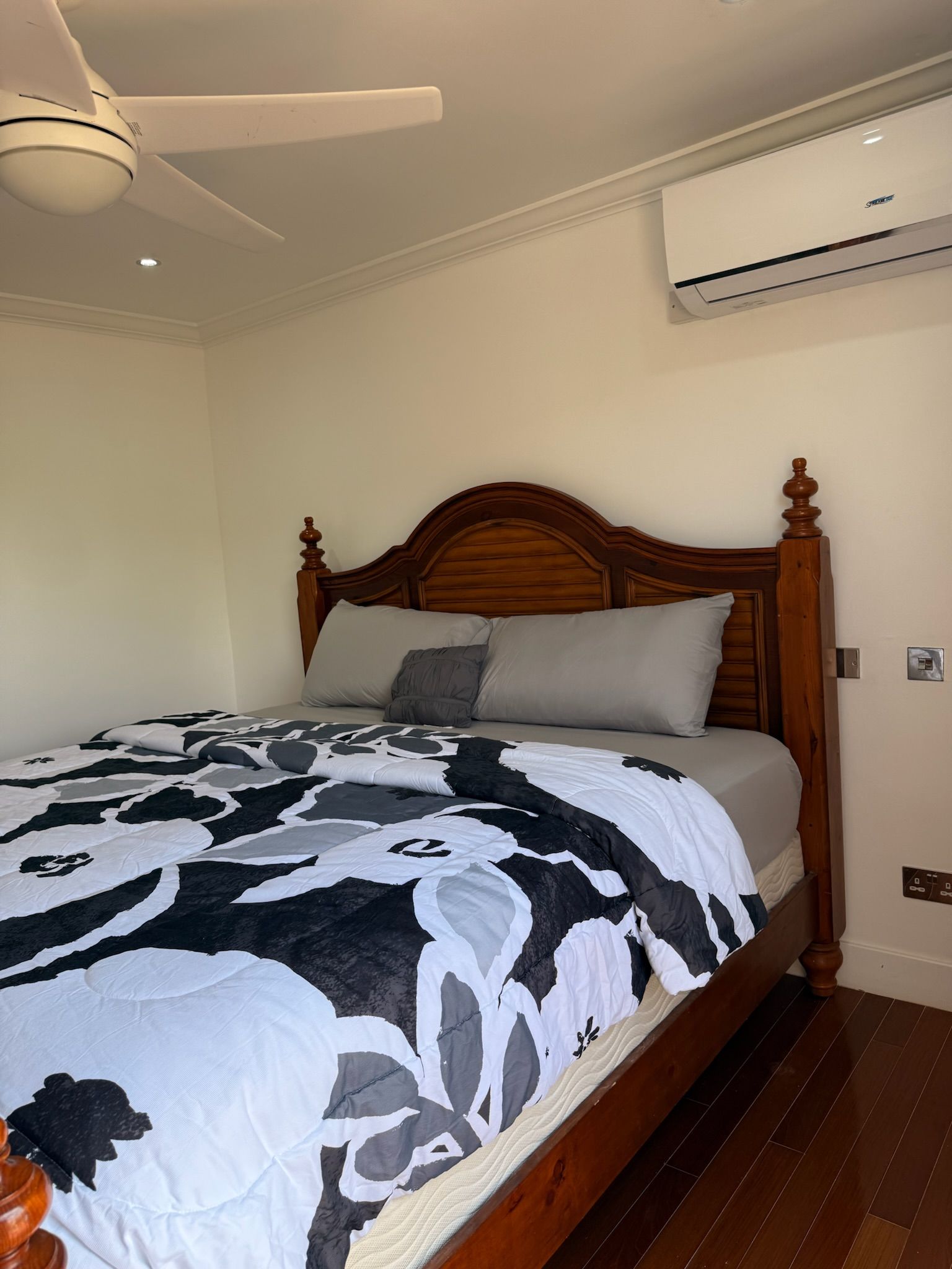 A bedroom with a wooden bed, a ceiling fan, and an air conditioning unit.