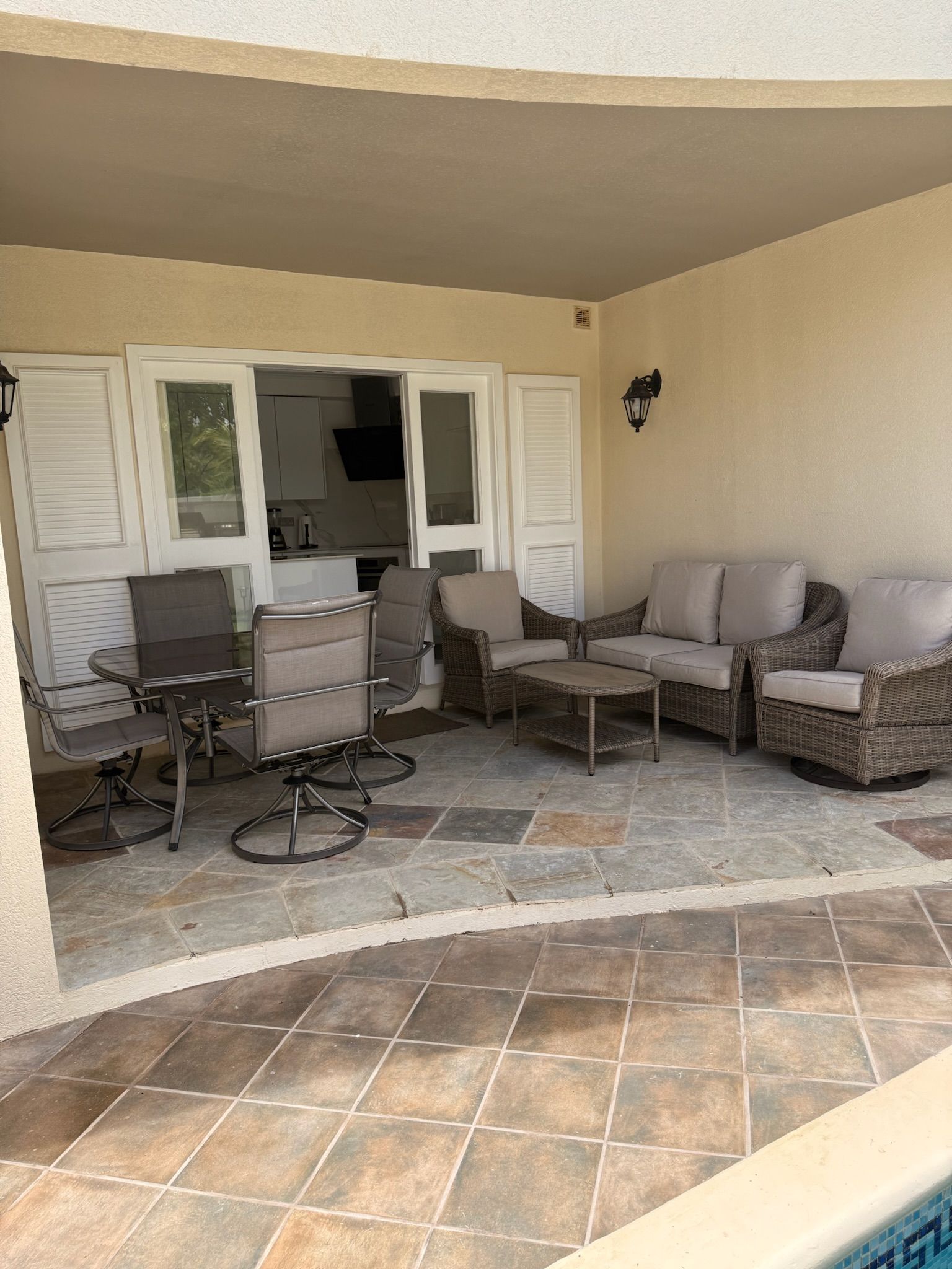 Een overdekt terras met een eettafel, stoelen, een bank en een bijzettafeltje.