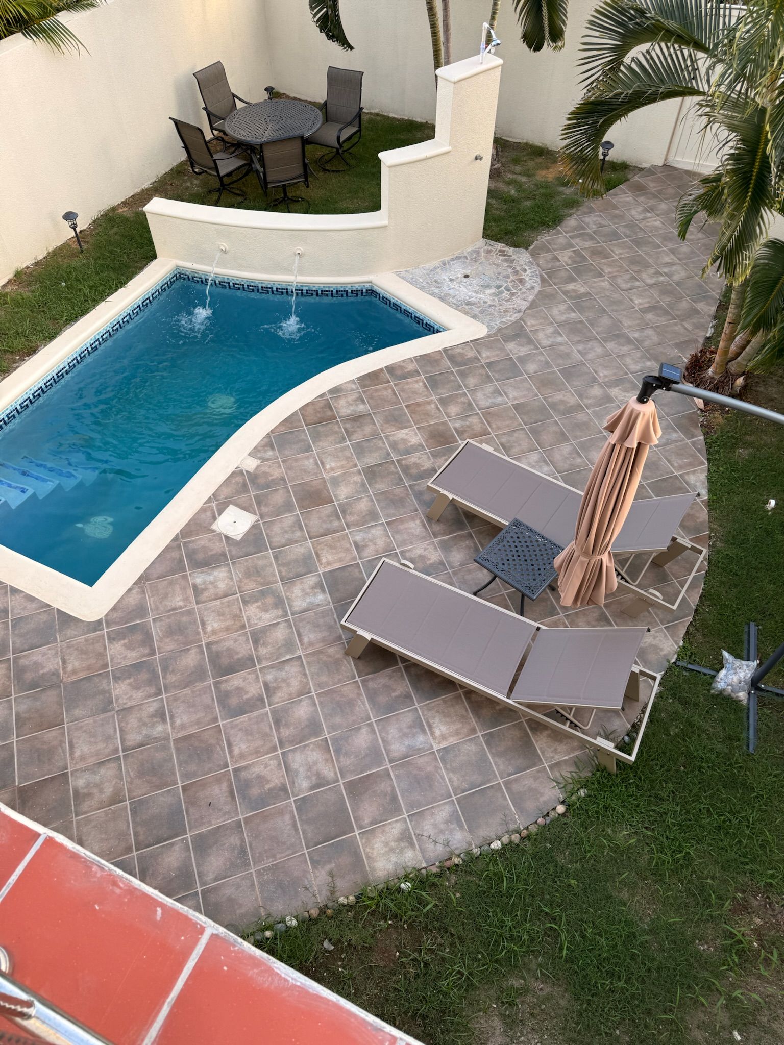 Una piscina con bordo piastrellato, sedie a sdraio e un tavolo con sedie.