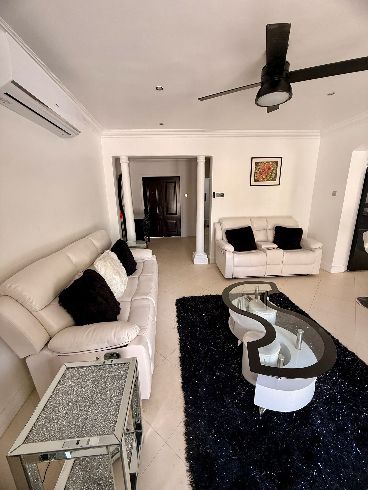Un salon moderne avec un canapé blanc, une table basse en verre et un tapis à poils longs noir.