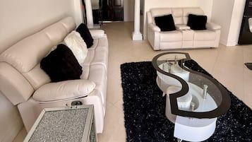 Un salon moderne avec un canapé blanc, une table basse en verre et un tapis à poils longs noir.
