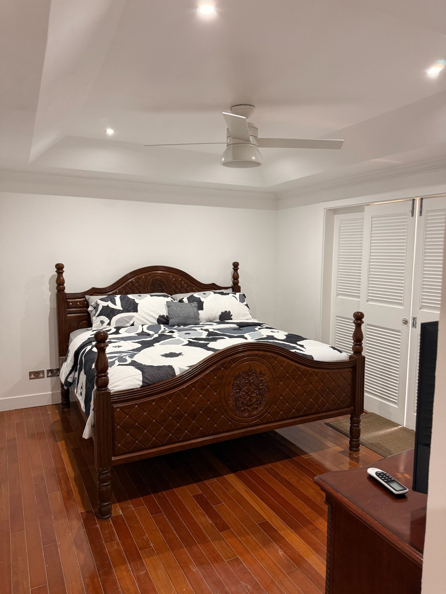 Een slaapkamer met een houten bed, een plafondventilator en een kledingkast met verstelbare deuren.